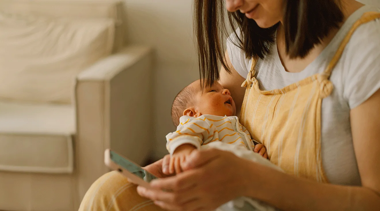 mom looking at smartphone while holding baby at home