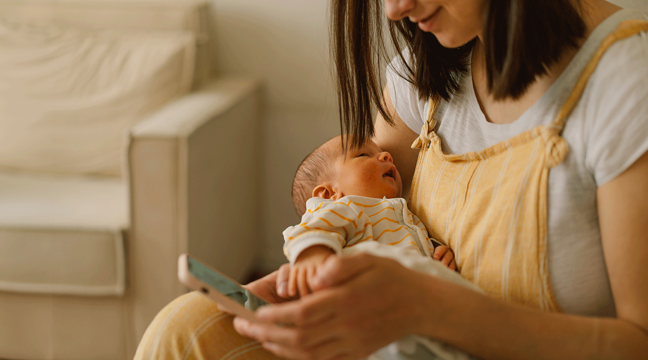 mom looking at smartphone while holding baby at home