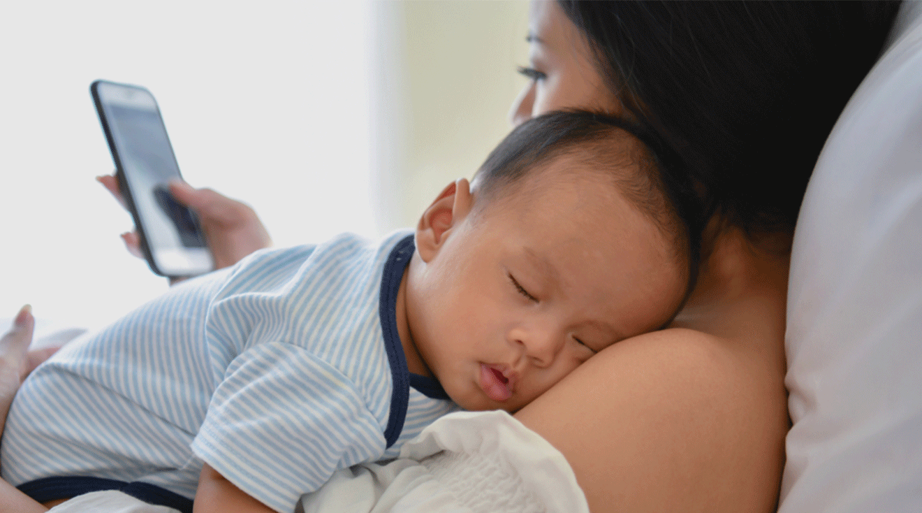 mom holding sleeping baby while looking at phone screen