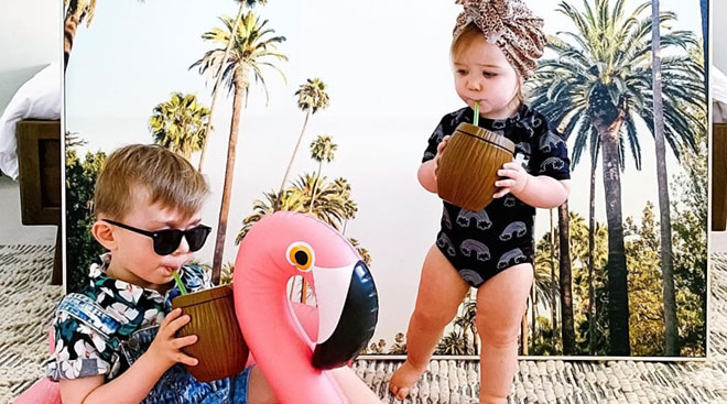 two toddlers against fake palm tree vacation backdrop 