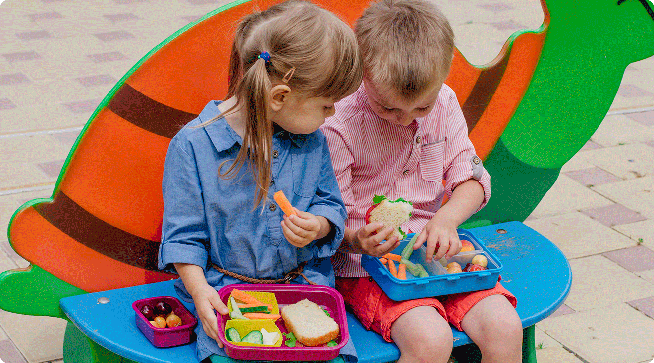 2 toddlers eating lunch out of lunch boxes