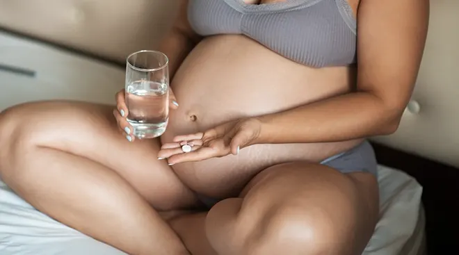 pregnant woman taking vitamins in bed with a glass of water