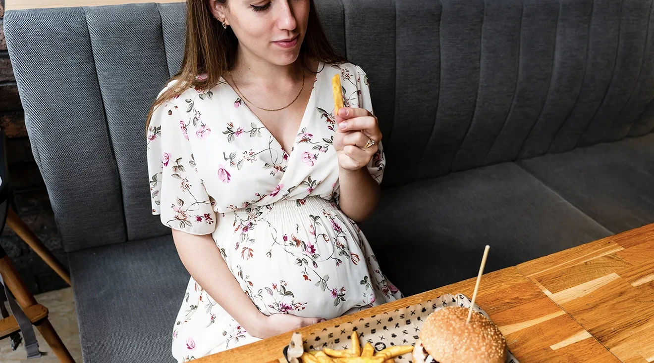 pregnant woman eating a burger and fries at restaurant 
