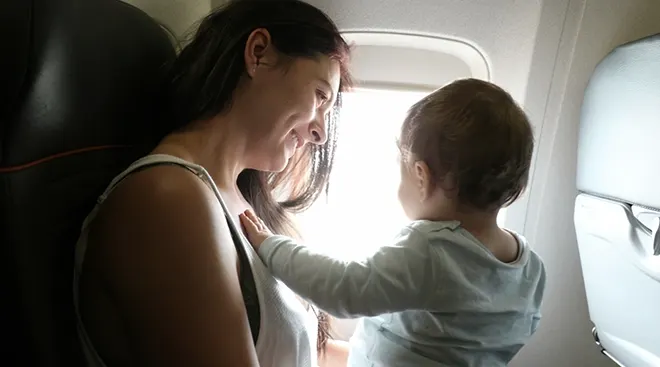 mother sitting on airplane with baby looking out window
