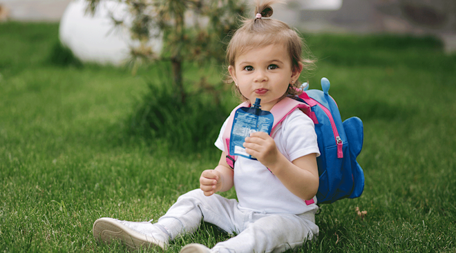 toddler eating a snack with backpack on outside