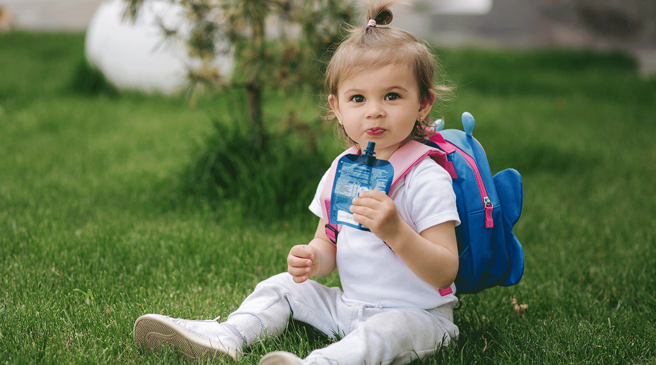 toddler eating a snack with backpack on outside