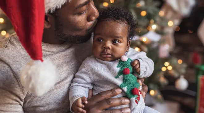 father kissing baby in front of christmas tree at home