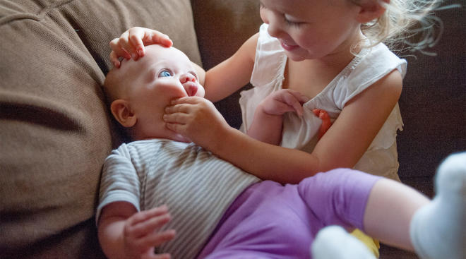 toddler with her baby sister, squishing her face