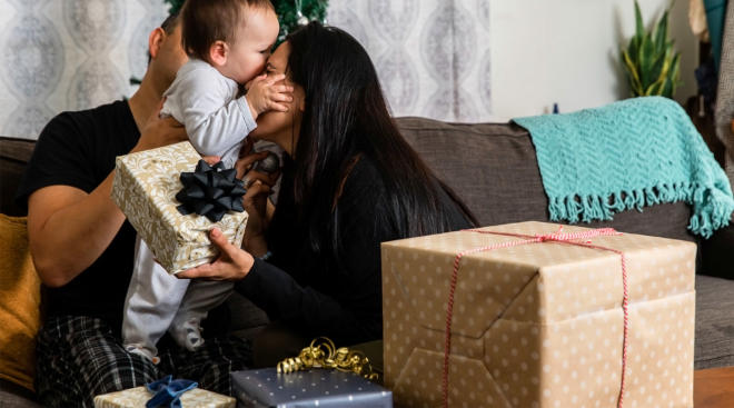 parents hugging baby on christmas morning with gifts nearby