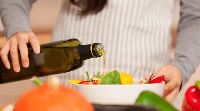 woman pouring olive oil onto vegetable salad