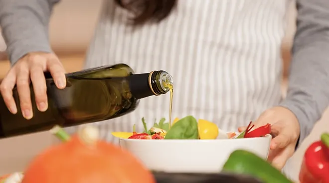 woman pouring olive oil onto vegetable salad