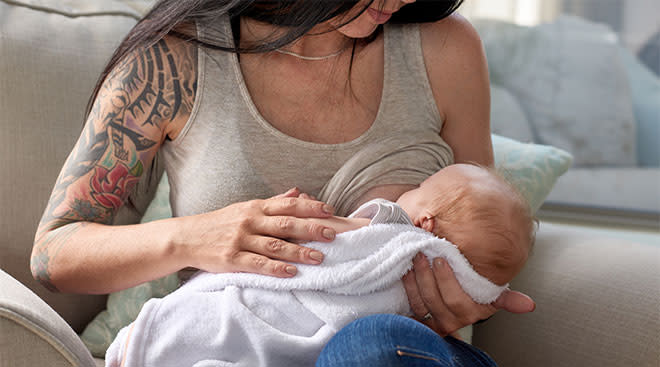 Mom with tattoos holding her baby and breastfeeding it. 