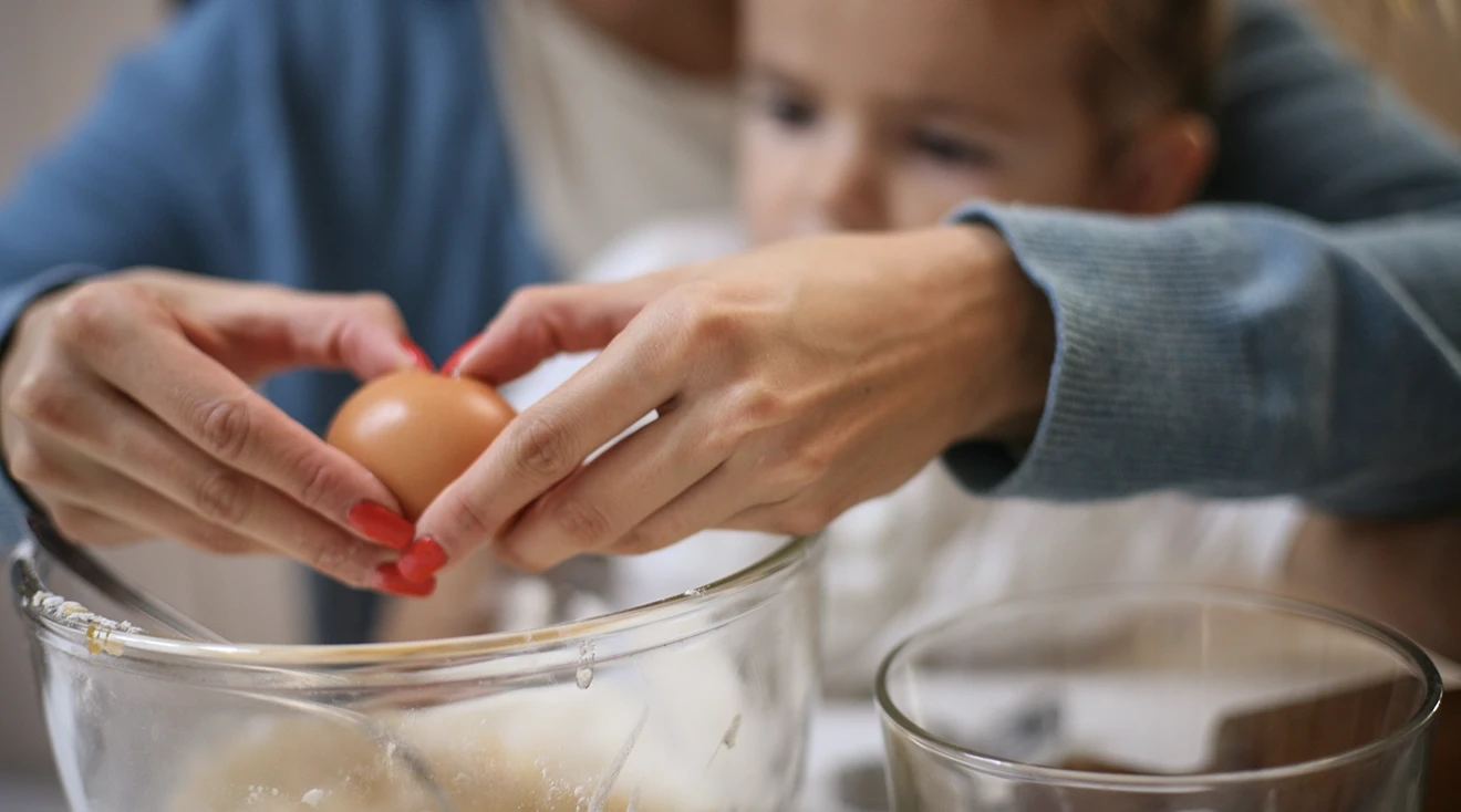 mother cracking an egg while baking with young daughter 