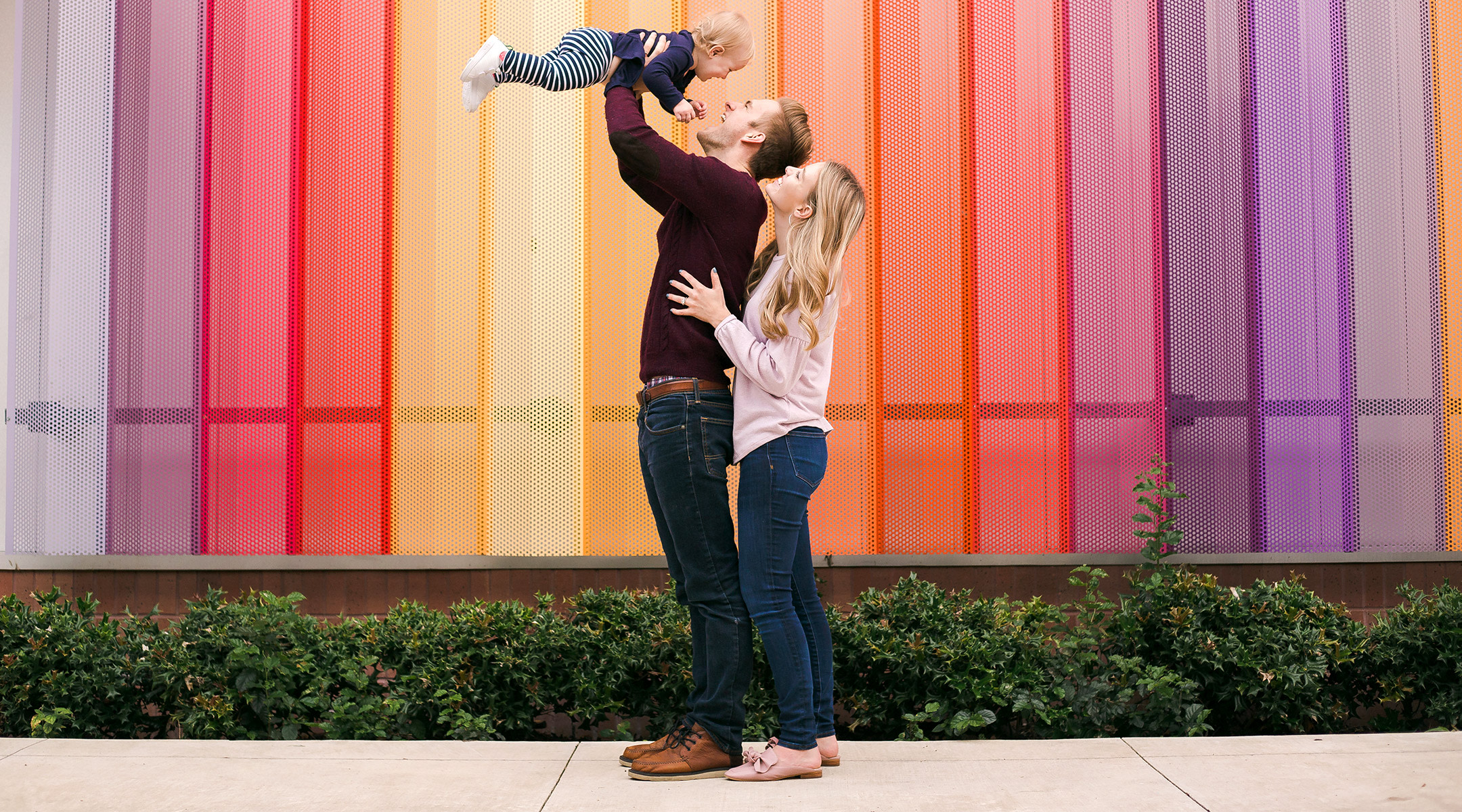 parents holding up baby in front of colorful background