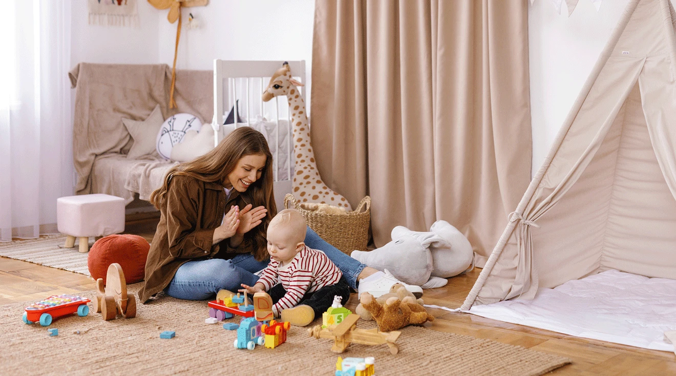 young nanny playing with baby in nursery room at home