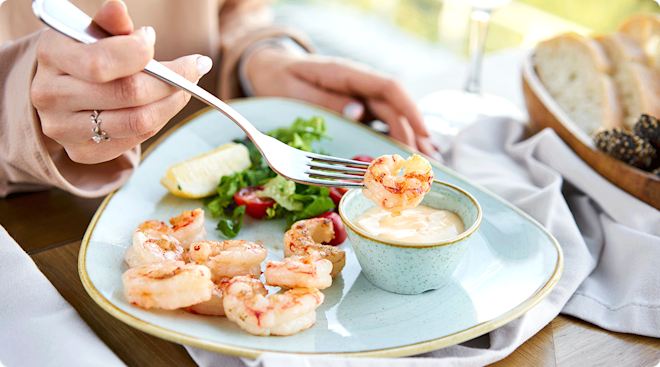 A woman eating grilled shrimp at a restaurant.