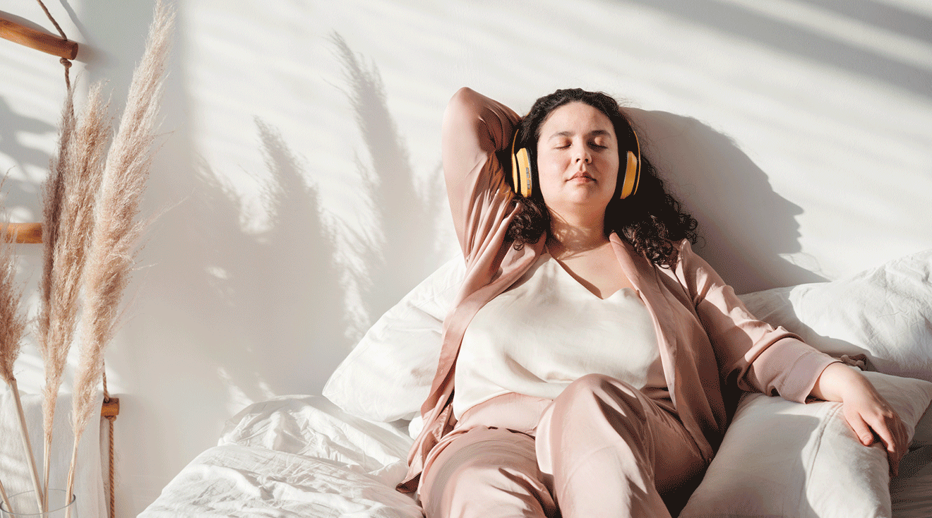 young woman wearing pajamas and headphones relaxing in bed