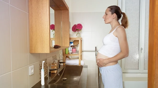 pregnant woman standing in the bathroom looking in the mirror
