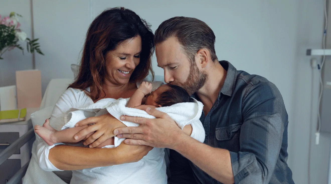 mother and father cuddling newborn baby in hospital bed after labor and delivery