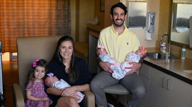 Parents sitting with identical triplets and their 3-year-old