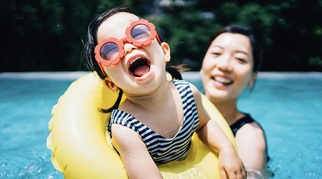 toddler wearing sunglasses in pool with mom during hot summer day