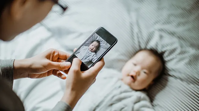 mother taking picture of baby on bed at home
