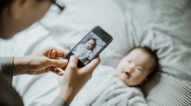 mother taking picture of baby on bed at home