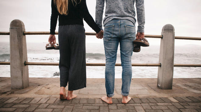 couple holding hands facing away on a pier by the water