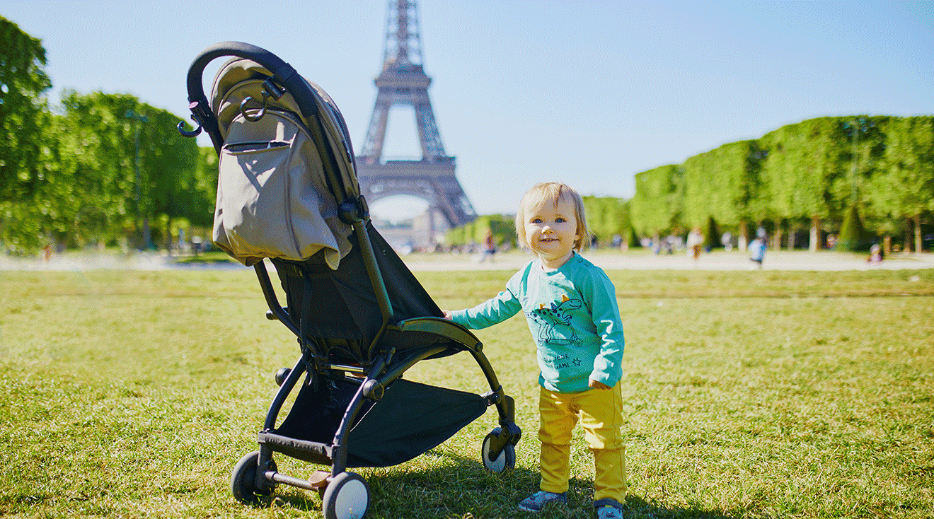 baby standing next to stroller in front of the eiffel towel in paris france
