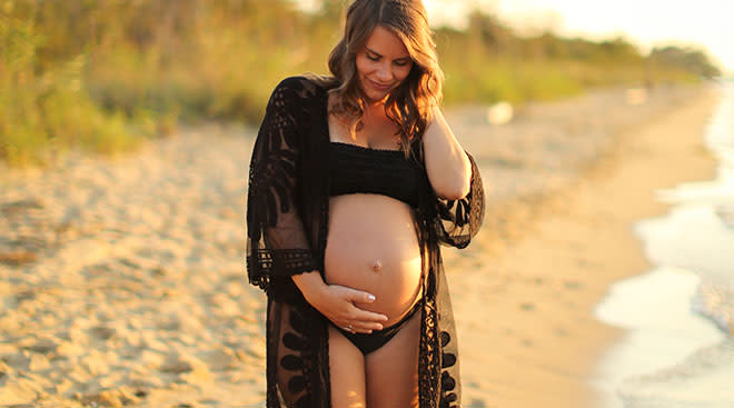Pregnant woman touching her belly by the beach.