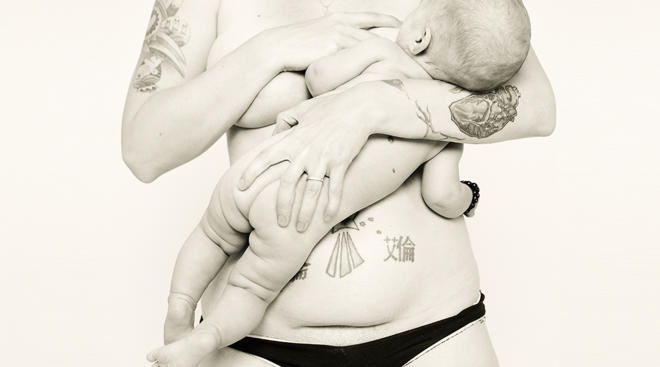 mom's postpartum body photographed while holding newborn and breastfeeding