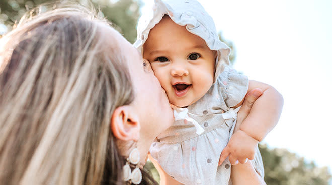 mom lifting happy baby wearing a bonnet into the air