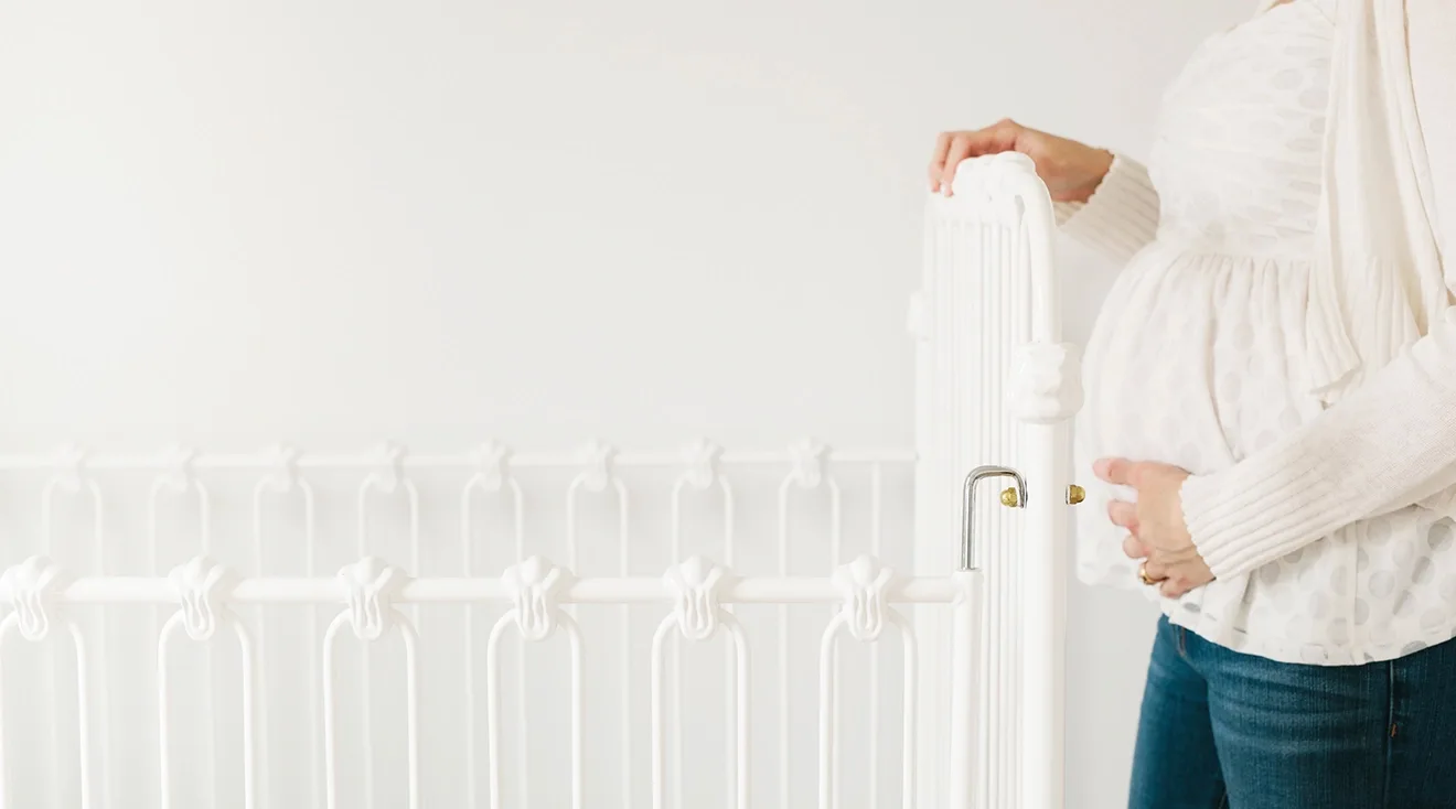 close up of pregnant woman standing near baby crib