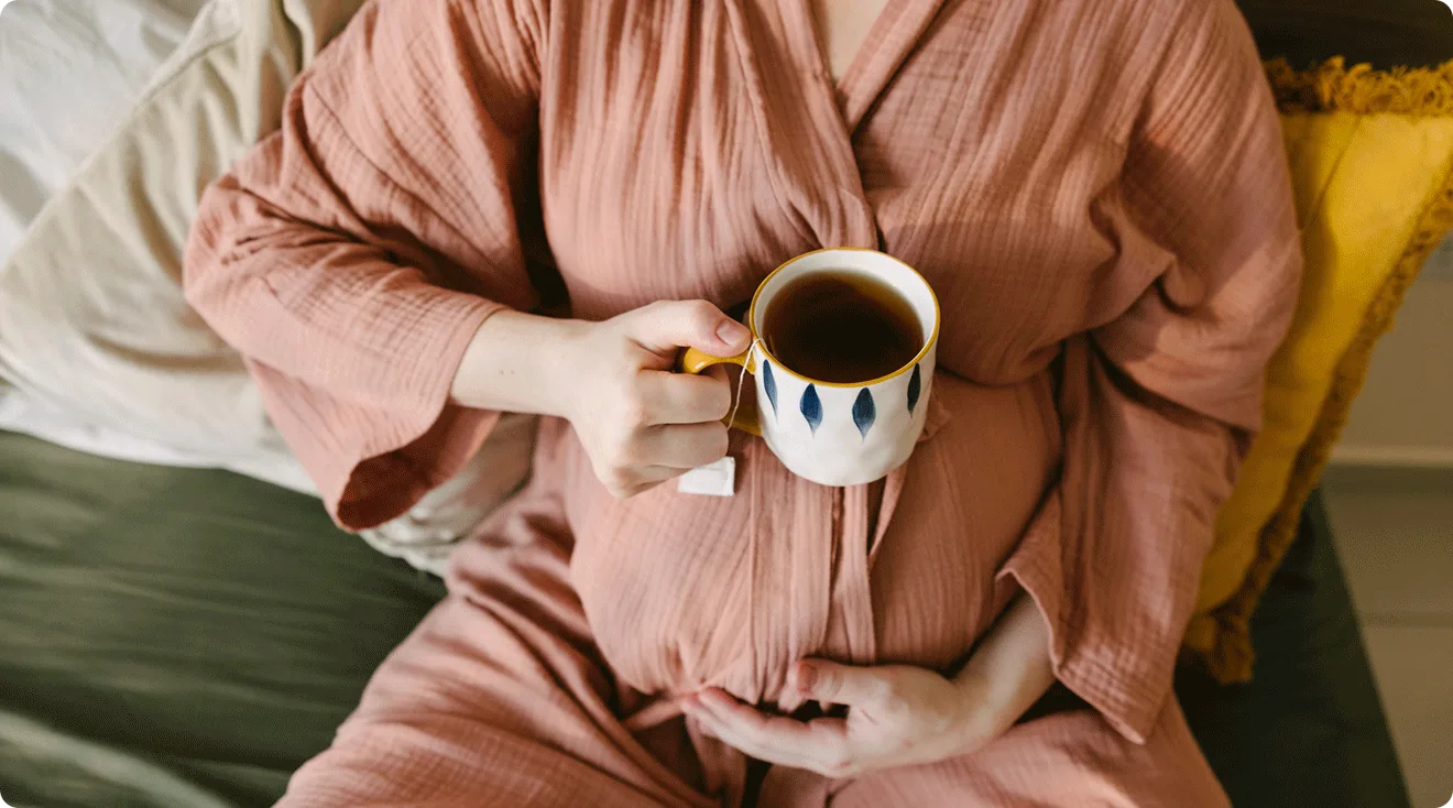 pregnant woman holding a cup of black tea at home