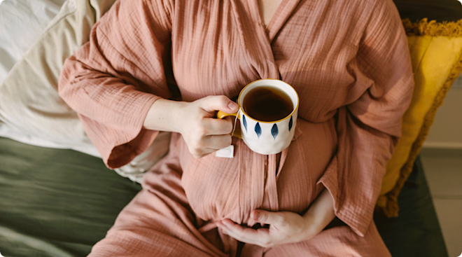 pregnant woman holding a cup of black tea at home