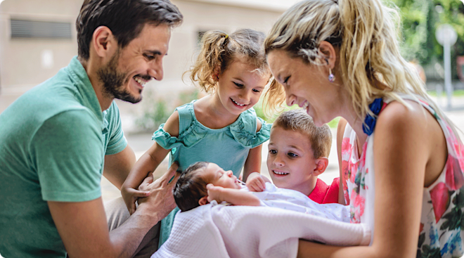 Happy parents showing their two small children their newborn baby sibling. 