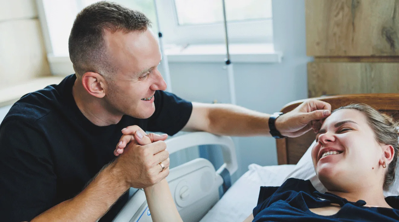 husband and wife smiling and holding hands during labor and delivery