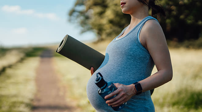 close up of pregnant woman holding yoga mat and water bottle outside