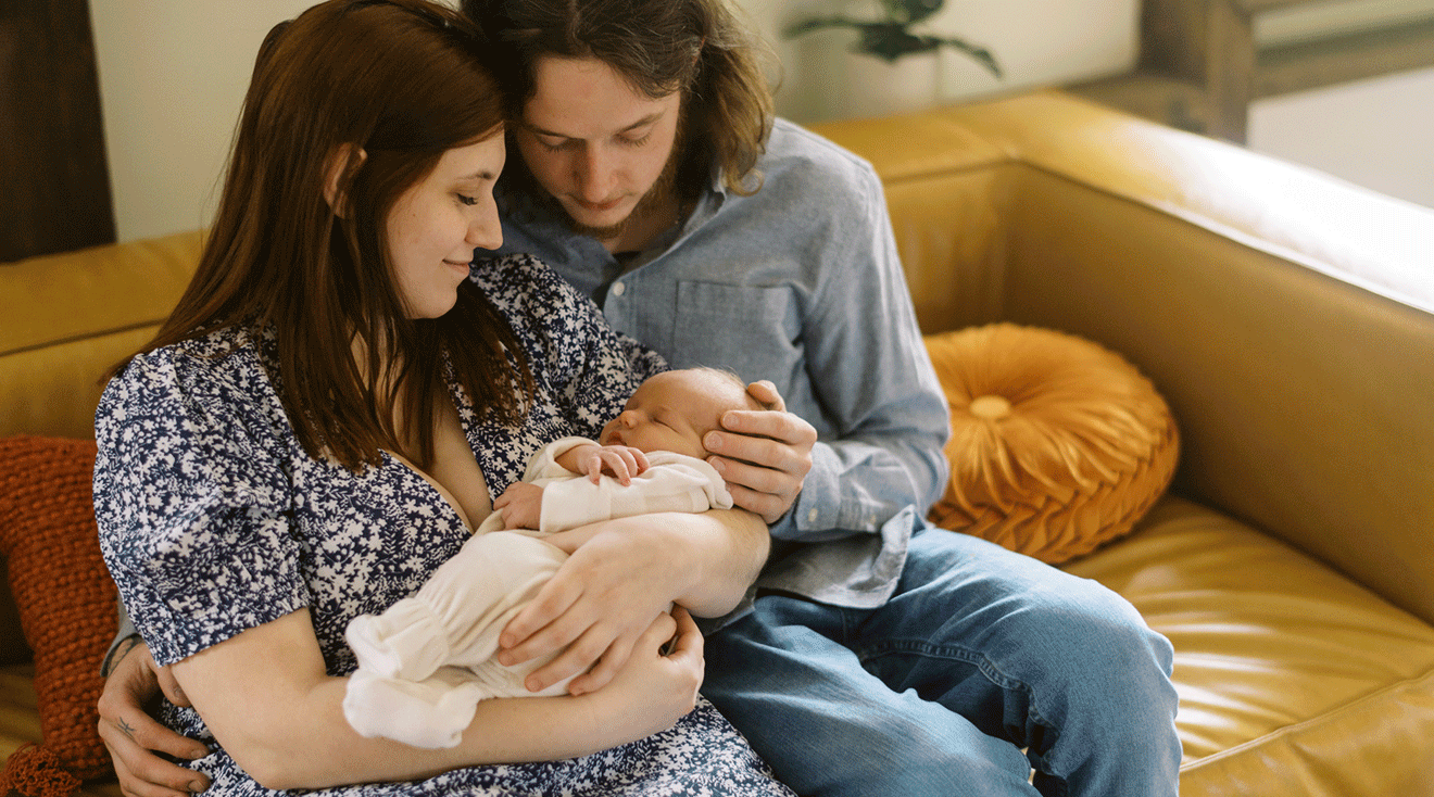 new parents holding newborn baby on couch at home