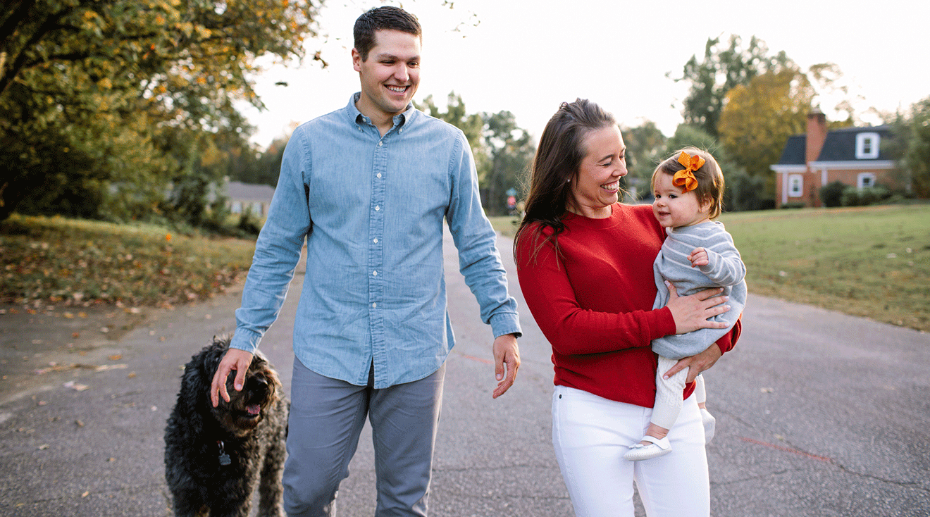 happy mom and dad walking in neighborhood with baby and dog