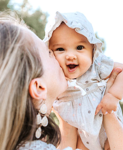mom lifting happy baby wearing a bonnet into the air