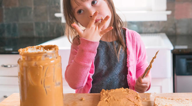 little girl making peanut butter sandwich and licking her hand