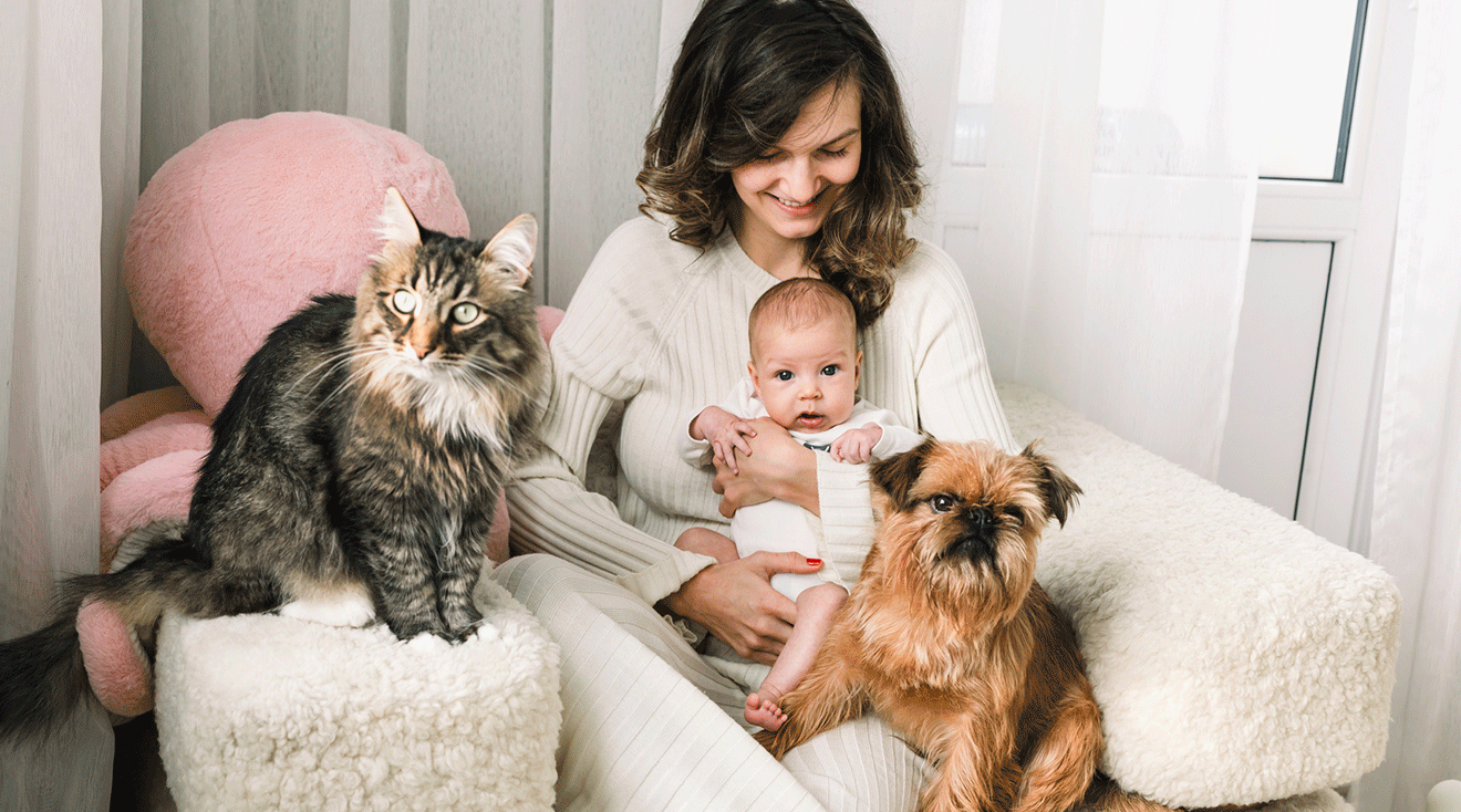 mom holding baby next to cat and dog at home