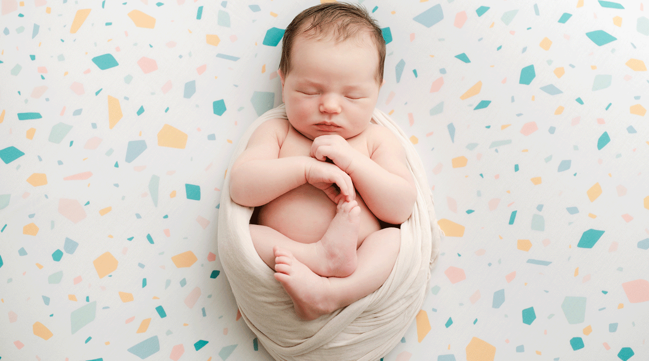 newborn baby swaddled in scrunch position on colorful background