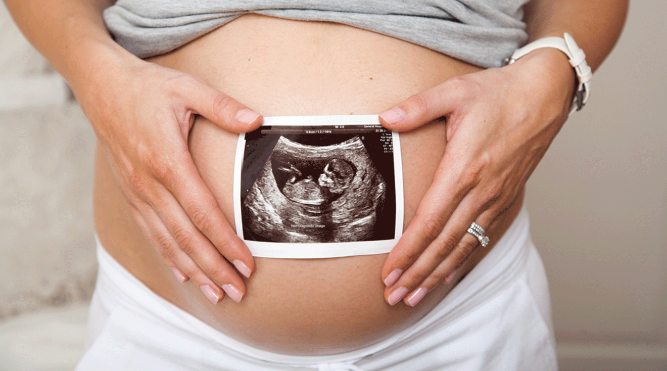 pregnant woman holding ultrasound photo in front of belly