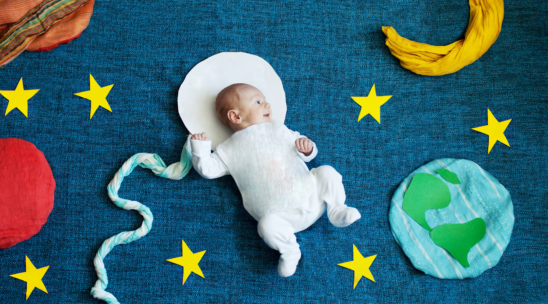 staged environment that shows newborn baby in space suit surrounded by stars and planets