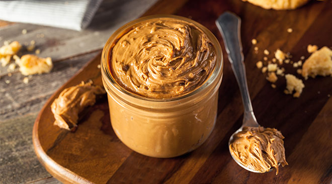 Open jar of peanut butter on wooden cutting board. 