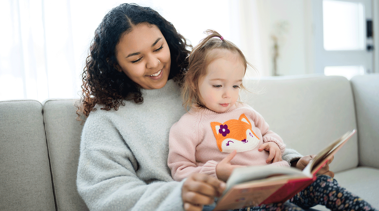 babysitter reading a book with toddler at home