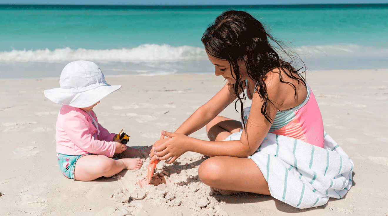 baby and big kid playing on the beach sunny summer day