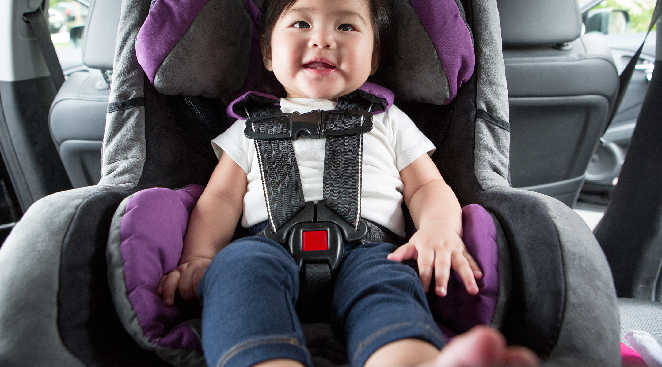 happy baby sitting inside car in a car seat